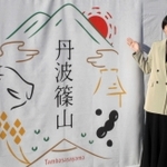 作者の岡田さんとブランドロゴ。「市名の周りに宝石があふれているイメージにした」という＝丹波篠山市北新町
