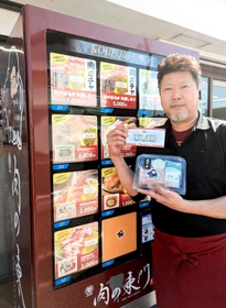 「肉ガチャ」がある冷凍牛肉自販機の横で、ステーキ肉や商品券を手にする東門昭喜社長＝丹波篠山市西新町