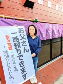 呼び文句を記した幕の横に立つ大地友代店主。観光客が撮影することもあるという＝丹波篠山市二階町