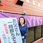 呼び文句を記した幕の横に立つ大地友代店主。観光客が撮影することもあるという＝丹波篠山市二階町