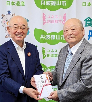 酒井隆明市長（左）に寄付金の目録を手渡す井関道夫さん＝丹波篠山市役所