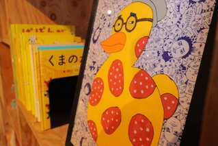 顔で画面を埋め尽くしたイラスト。本の色と合わせて作品を展示する＝マミムメモ・ブックブック