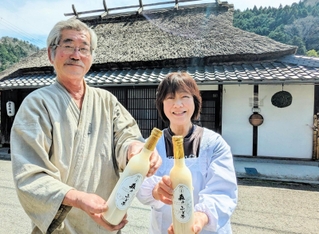 農家民宿「森の風土」の前で、どぶろく「森のふど子」を手にする唐渡たかねさん（右）と民宿オーナー森田忠さん＝丹波篠山市川原