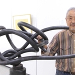 鉄製の彫刻「横たわる女」と作者のジュン・タンバこと塚脇淳さん＝植野記念美術館