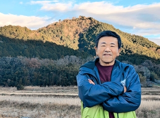 高城山を背にした山口喜昭さん。江戸時代、山には藩有林があり、収穫されたマツタケが幕府へも献上されたという＝丹波篠山市内