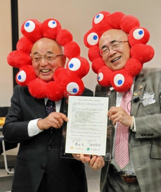 「美食街道」の協定書を手にする酒井隆明市長（左）と溝畑宏理事長。万博の公式キャラクターのかぶりものを身に着ける＝丹波篠山市北新町