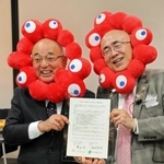 「美食街道」の協定書を手にする酒井隆明市長（左）と溝畑宏理事長。万博の公式キャラクターのかぶりものを身に着ける＝丹波篠山市北新町