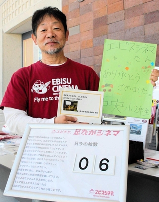 子どもからの礼状を手にする近兼拓史さん。映画館には取り置き枚数を記したボードも設置されている＝丹波篠山市今田町今田新田