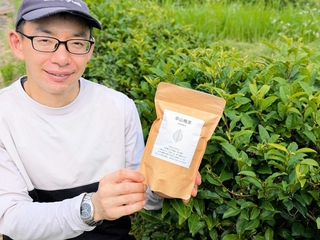 チャノキの前で「草山晩茶」のパッケージを手にする松本修さん＝丹波篠山市遠方