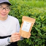 チャノキの前で「草山晩茶」のパッケージを手にする松本修さん＝丹波篠山市遠方
