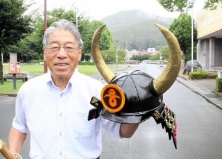 黒井城跡をバックに自作のかぶとを掲げる吉住孝信さん＝丹波市春日町黒井