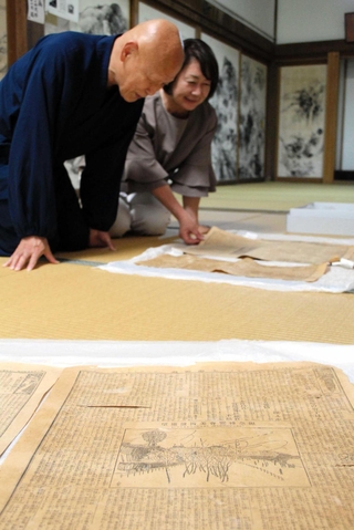 びょうぶから見つかった新聞を見る日置義紹住職（左）ら＝丹波市氷上町御油