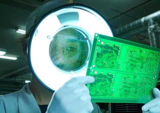 １枚ずつ電子基板をチェックする従業員。最新の技術と人の目による入念な確認が品質の高さを守っている＝丹波市氷上町石生