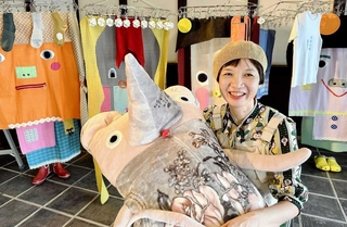 自作のぬいぐるみアートを抱き、洗濯物をイメージした新作「素風快晴」の前に座る造形作家あさうみまゆみさん＝丹波篠山市河原町