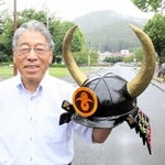 黒井城跡をバックに自作のかぶとを掲げる吉住孝信さん＝丹波市春日町黒井