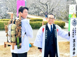 黒豆を入れた俵やサヤ付きの枝などを背負った小田垣昇社長（左）と福井正一社長＝丹波篠山市北新町