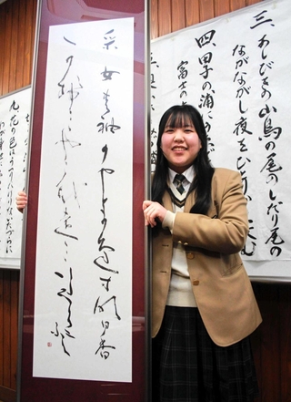 受賞作品を手にする青木環さん。後ろには百人一首をしたためた作品が並ぶ＝丹波市氷上町黒井