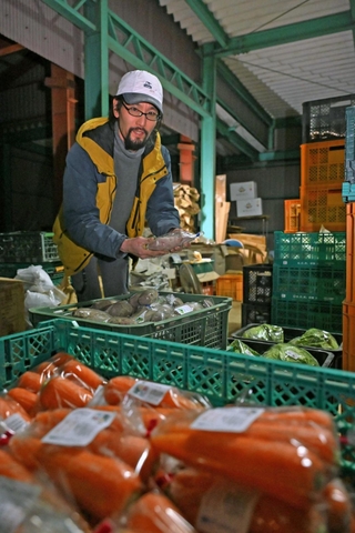 若手農家らが持ち寄った野菜に囲まれるおひさんファームの広澤正道さん。出荷に向け作業を進める＝丹波市市島町北奥