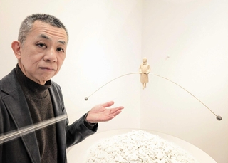 新作の横に立つ古巻和芳さん。白い山はガレキの象徴。少女には、困難な道を行くさまざまな人の姿を投影したという＝エンギャラリー芦屋