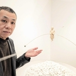 新作の横に立つ古巻和芳さん。白い山はガレキの象徴。少女には、困難な道を行くさまざまな人の姿を投影したという＝エンギャラリー芦屋