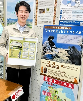 市役所の署名コーナーで、署名用紙を投入する箱を手にする市職員と、河合雅雄さんを顕彰する講演会のＰＲポスター＝丹波篠山市北新町