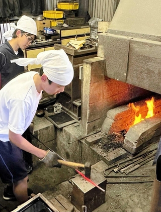 赤く熱した鉄の棒をハンマーで鍛える藤田真嗣さん（手前）＝丹波篠山市今田町下立杭