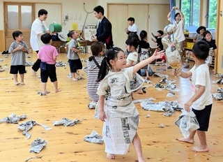 新聞紙で作った衣装を着たり、丸めて投げたりして遊ぶ園児ら＝こんだ認定こども園