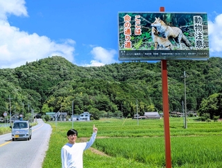 野生動物が関係する交通事故の防止を訴える看板と阪下伸二さん＝丹波篠山市西谷