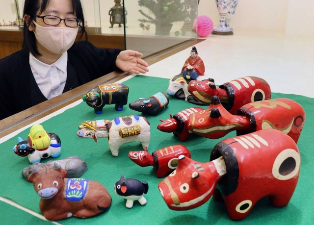 赤べこ（右）など各地の牛の郷土玩具を紹介する横山奈央子さん＝加古川市加古川町粟津