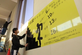 階段の利用を促すため、ポスターを掲示する学生＝ＪＲ東加古川駅