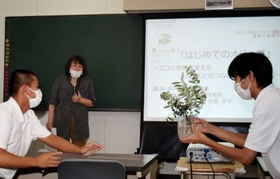 生徒にオリーブの実物を示しながら、歴史や用途について解説する中西テツさん（中央）＝東播工業高校