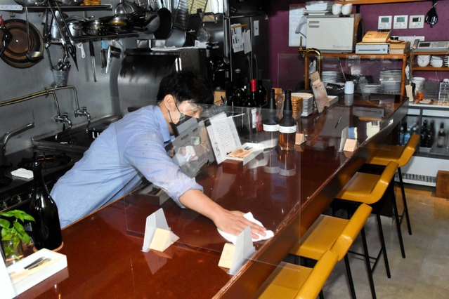 開店に向け、間仕切りが設けられたカウンターをアルコールで拭く藤沢大祐さん＝加古川市平岡町新在家２