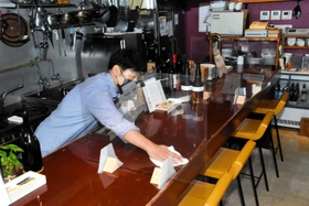 開店に向け、間仕切りが設けられたカウンターをアルコールで拭く藤沢大祐さん＝加古川市平岡町新在家２