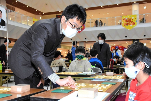 指導対局で子どもにアドバイスを送る稲葉陽八段（手前左）や久保利明九段（奥）＝ニッケパークタウン