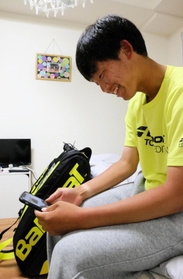 激しい練習を終え、寮で両親と携帯のテレビ電話で会話する副主将の高畑里樹さん。壁には東京のテニス仲間が書いてくれた寄せ書きが掛かる＝加古川市内