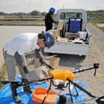 特殊なコーティングをした種もみをドローンに補充する共同防除隊のメンバー＝加古川市八幡町上西条