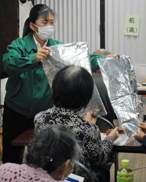 高齢者に防寒用シートを比べてもらう横山恭子さん。片方は安価だがシャカシャカと音が＝加古川市西条山手２