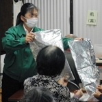 高齢者に防寒用シートを比べてもらう横山恭子さん。片方は安価だがシャカシャカと音が＝加古川市西条山手２