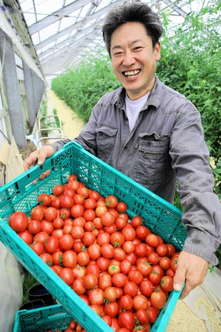 収穫した「プレミアムトマト」を前に笑顔を見せる松井農園の松井義輝さん＝稲美町加古