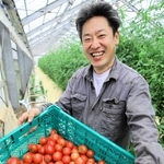 収穫した「プレミアムトマト」を前に笑顔を見せる松井農園の松井義輝さん＝稲美町加古