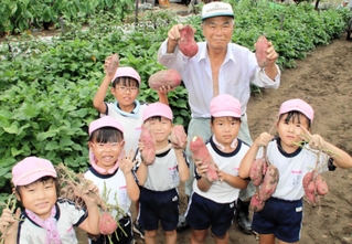 掘り出した芋を手に、子どもたちと笑顔を見せる隅野さん＝加古川市尾上町