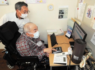 ＮＰＯ法人の事務所で働く高田耕志さん（手前）。助成制度のおかげで安心してヘルパーの介助が受けられる＝加古川市尾上町池田