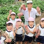 掘り出した芋を手に、子どもたちと笑顔を見せる隅野さん＝加古川市尾上町