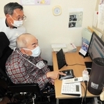 ＮＰＯ法人の事務所で働く高田耕志さん（手前）。助成制度のおかげで安心してヘルパーの介助が受けられる＝加古川市尾上町池田