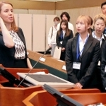 ハリマ化成のカルメン中村広報グループ長（左端）から株主総会の会場の説明を受ける学生ら＝加古川市加古川町溝之口