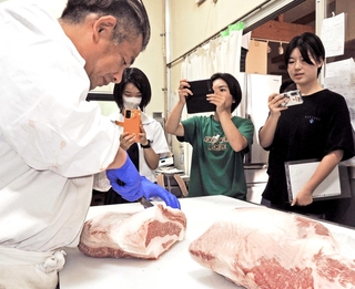 精肉加工会社「福良」の肉職人（左）の包丁さばきを動画撮影する加古川東高校の生徒たち＝加古川市志方町細工所
