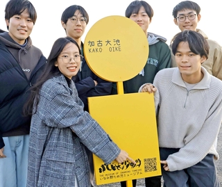 「ため池ＧＯ！」のＱＲコードが記された看板と、開発に参加する明石高専の学生たち。看板はバス停をイメージした＝稲美町加古、加古大池