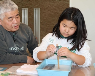 砥石や耐水性の紙やすりで滑石を削り、勾玉を作る参加者＝播磨町大中１、県立考古博物館