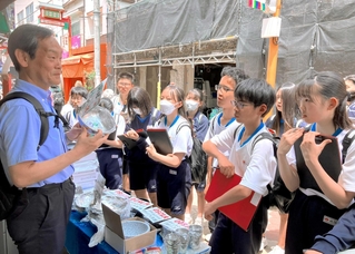 韓国の金属製食器について氷丘中２年生に説明する郭辰雄さん（左）。「日本とは使い方やマナーも違うが、それぞれに合理性がある」＝大阪コリアタウン