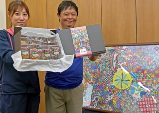 包装紙を使った商品を持つ森隆〓さん（右）と支援員の山本侑季さん。額に収まるのは森さんが城崎温泉で見た景色から着想を得た絵＝加古川市別府町新野辺　※〓は「まだれ」に「黄」